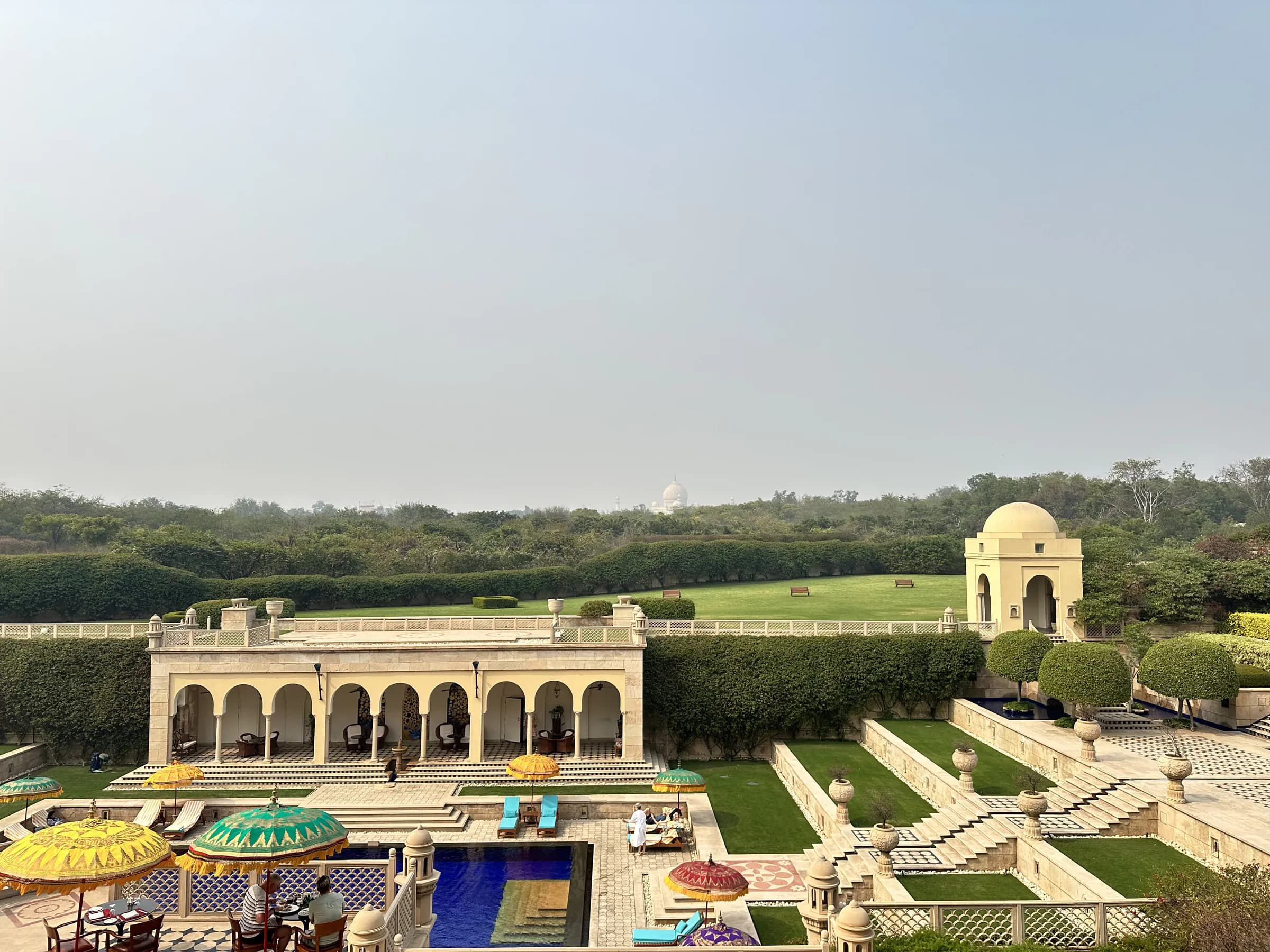 Los jardines en terrazas, el pabellón de la piscina y las sombrillas de The Oberoi Amarvilas, con el Taj Mahal pequeño en el horizonte brumoso, más allá de los árboles