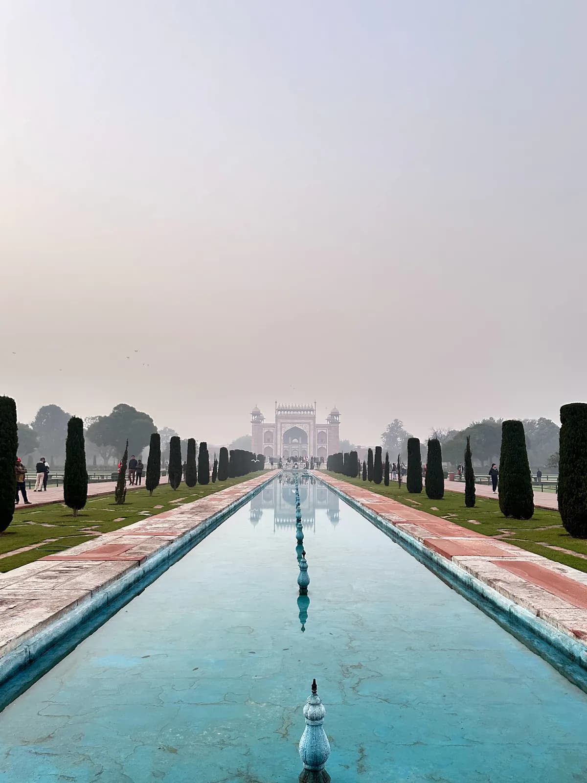 El largo canal de agua de los jardines del Taj Mahal al amanecer, mirando de vuelta hacia la puerta de arenisca roja