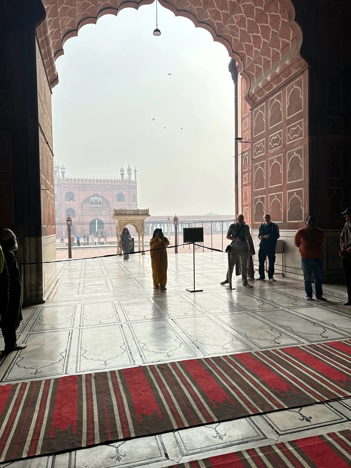 Vista desde debajo de un arco festoneado de la sala de oración de la Jama Masjid, a través del patio de mármol hasta la puerta del fondo