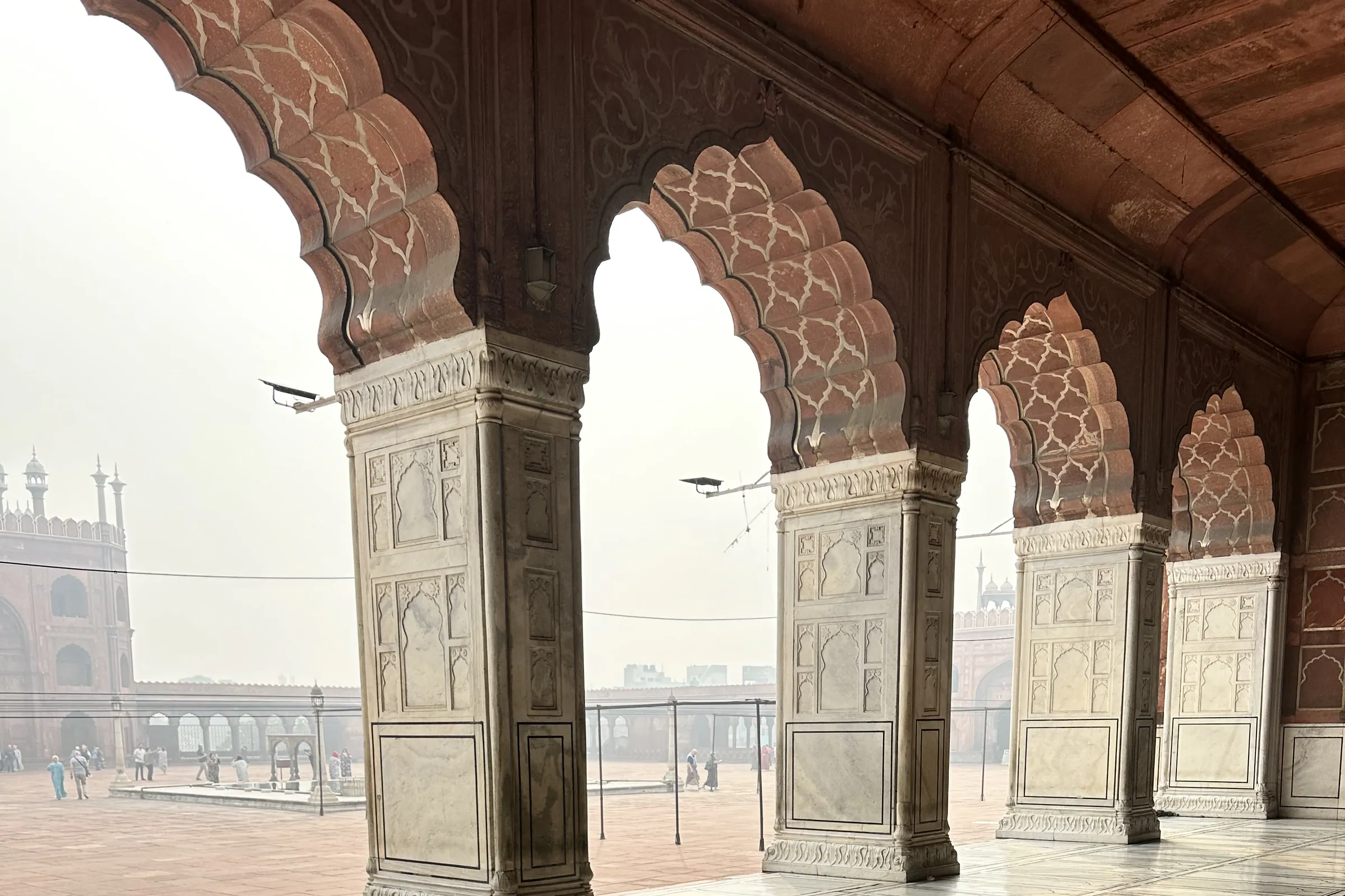 Arcos festoneados de arenisca roja sobre pilares de mármol tallado a lo largo de la sala de oración de la Jama Masjid, en la Vieja Delhi, sobre un suelo de mármol blanco con incrustaciones de líneas negras