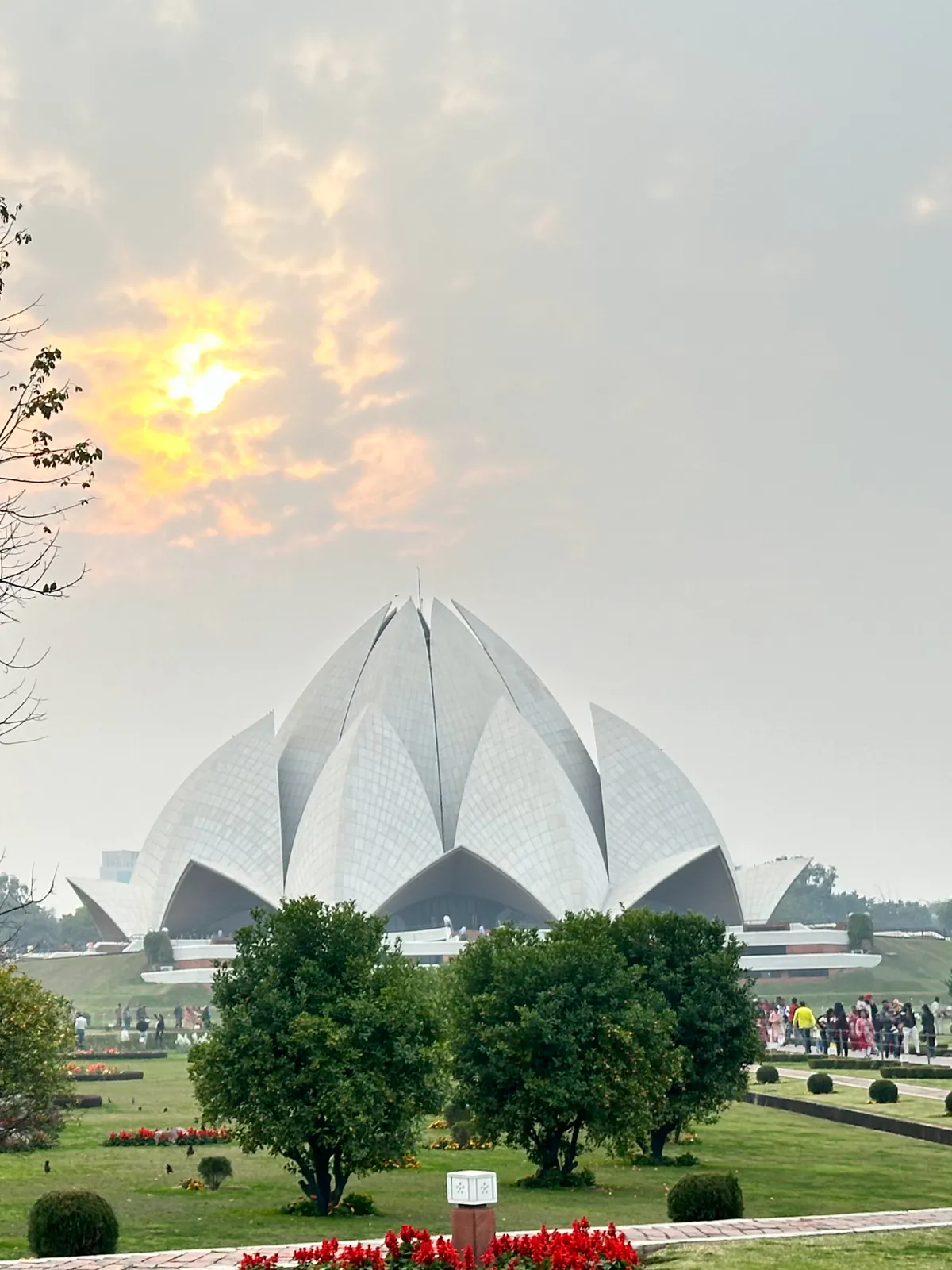 Los pétalos blancos del Templo del Loto, la Casa de Adoración bahaí de Delhi, tras árboles y céspedes en la bruma de la tarde