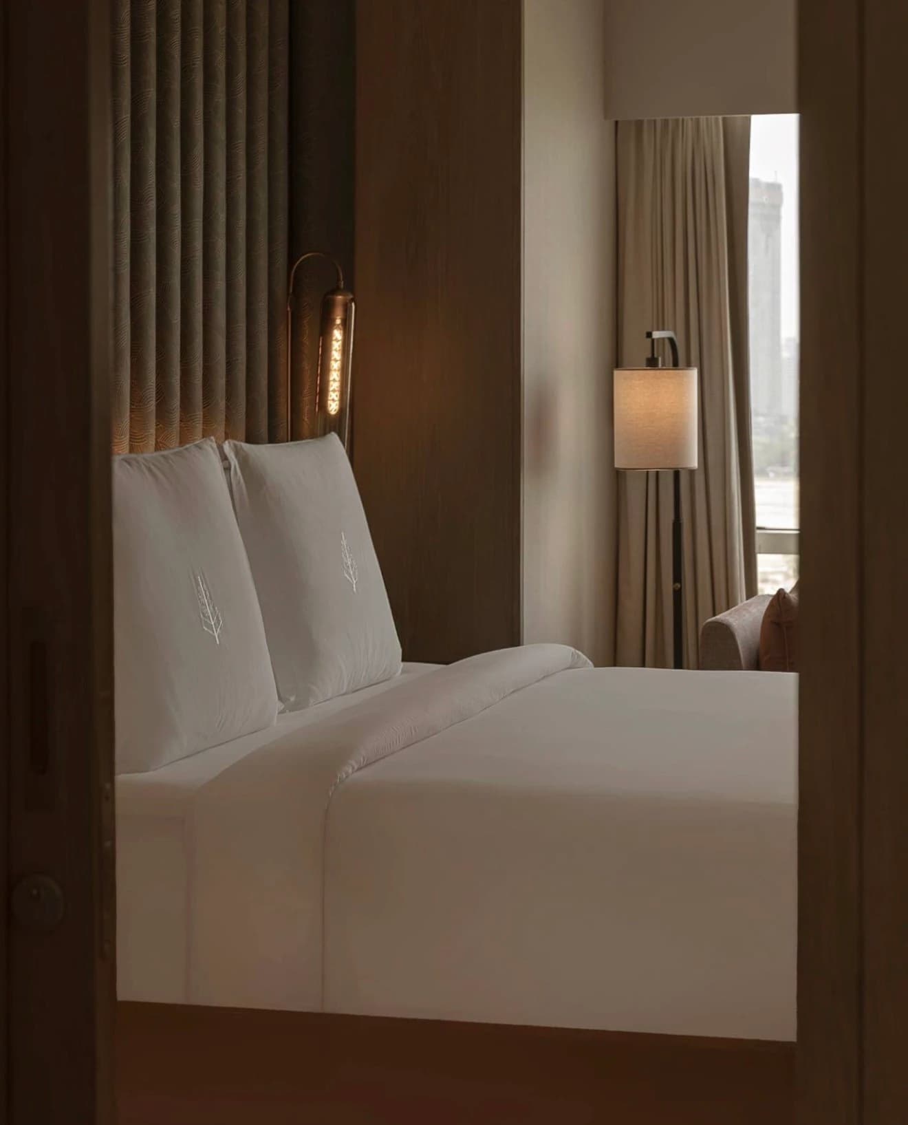 Una habitación de Four Seasons Hotel Mumbai vista desde la puerta: una cama blanca con almohadas bordadas, una lámpara y una ventana a la ciudad