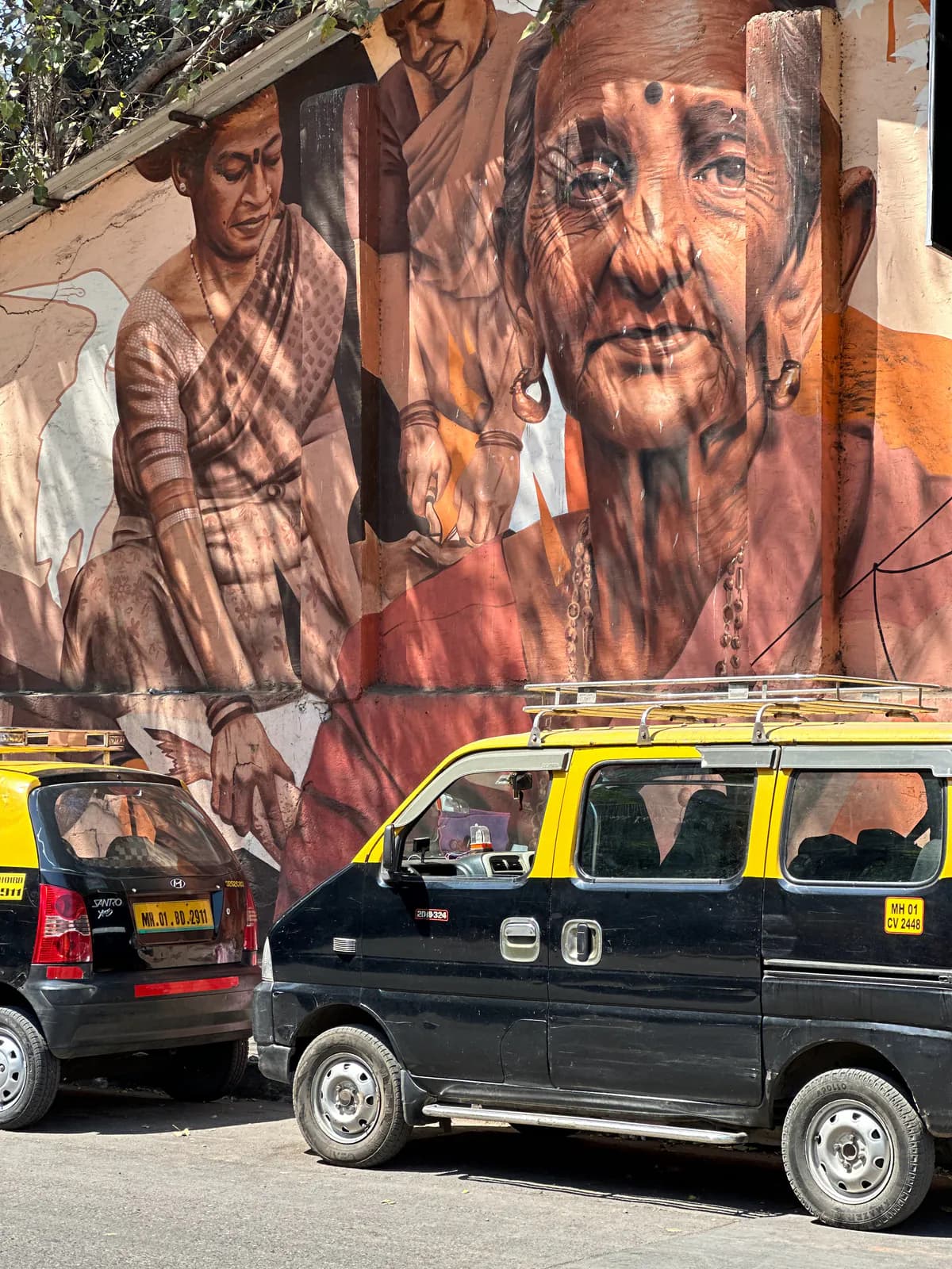 Taxis negros y amarillos de Mumbai aparcados bajo un gran mural callejero de dos mujeres