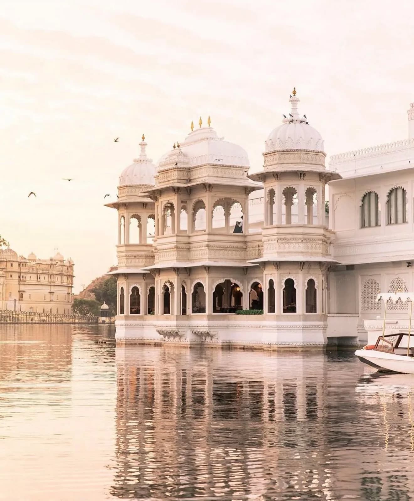 Los pabellones blancos con cúpulas de Taj Lake Palace se alzan sobre el lago Pichola, con el Palacio de la Ciudad en la orilla al fondo