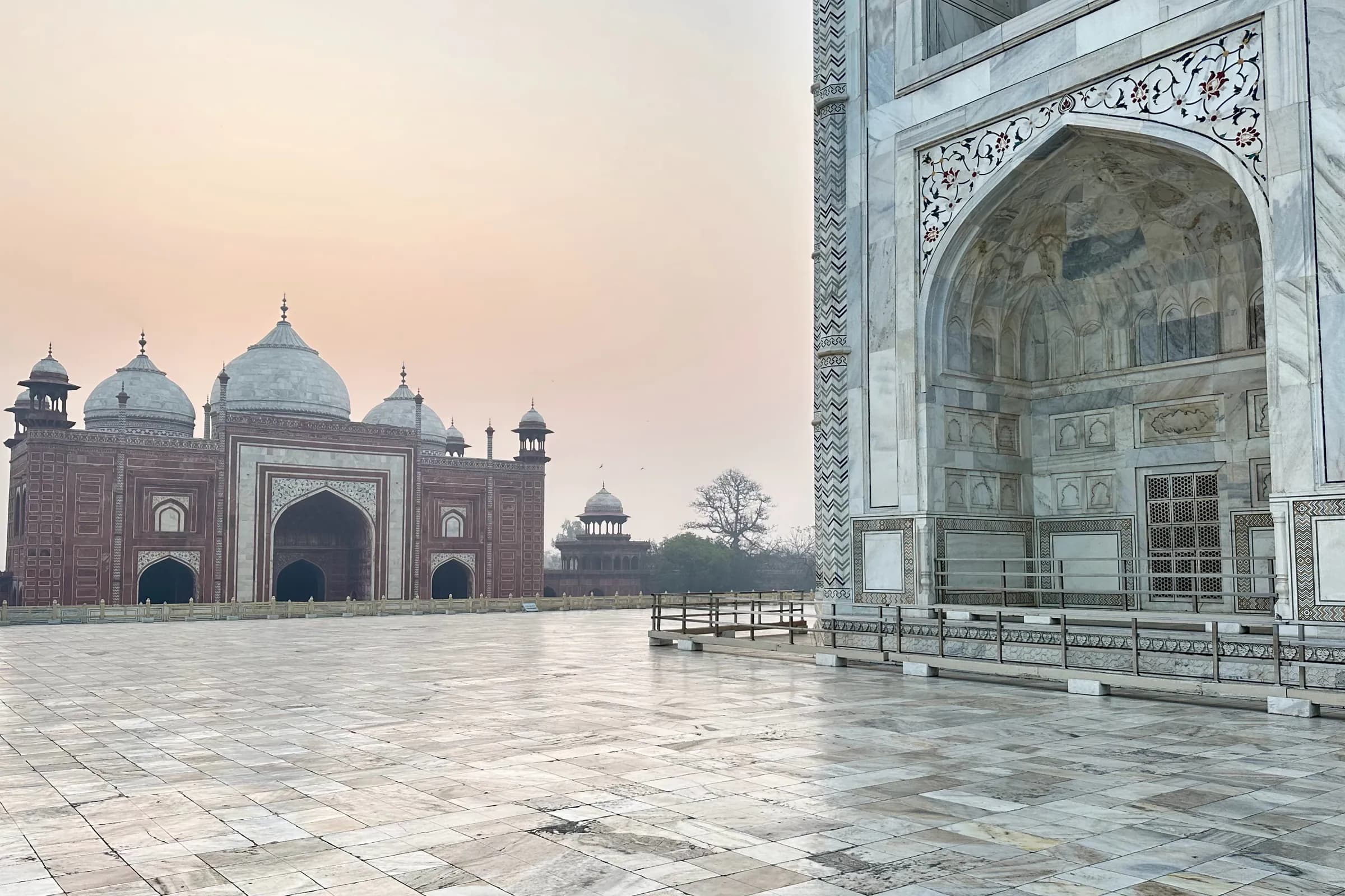 La mezquita de arenisca roja junto al Taj Mahal y el costado de mármol del mausoleo, bajo la luz rosada del amanecer