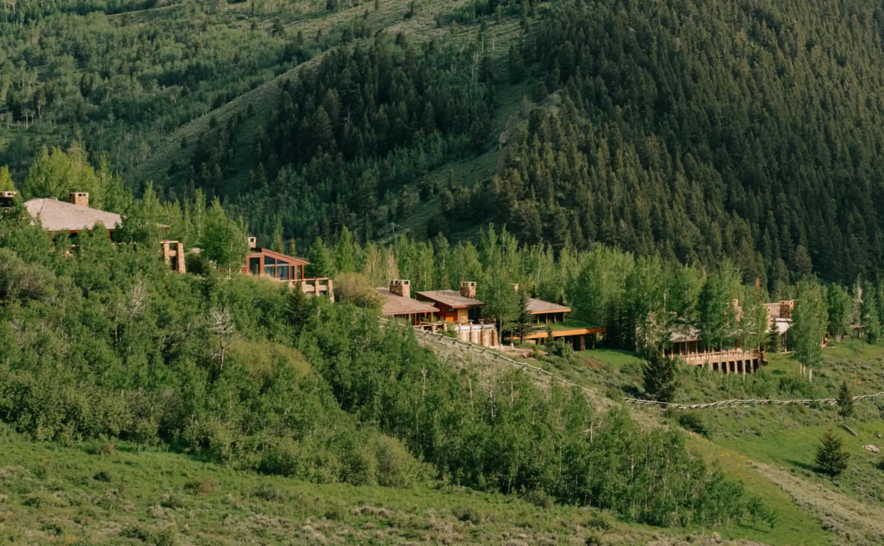 The Amangani residences among the aspens above Jackson Hole, low shingled roofs and stone chimneys set against the treeline.