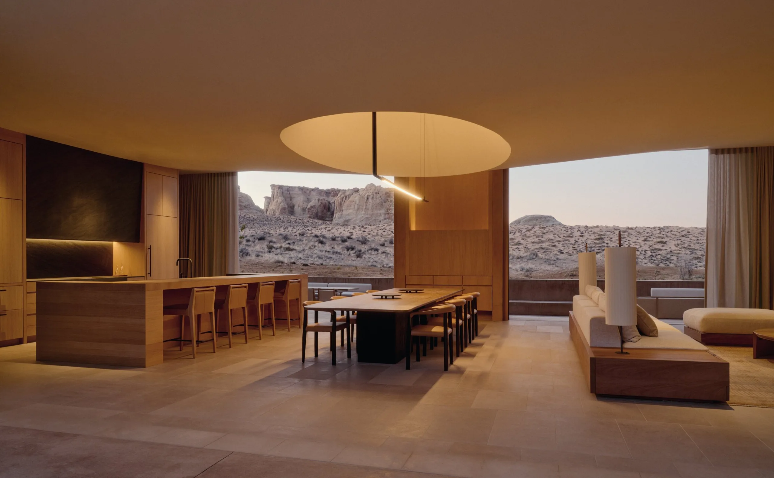 The living and dining room of a six-bedroom Amangiri residence, an open kitchen and long table beneath a floating ceiling, glazed the full width to the Utah rock beyond.