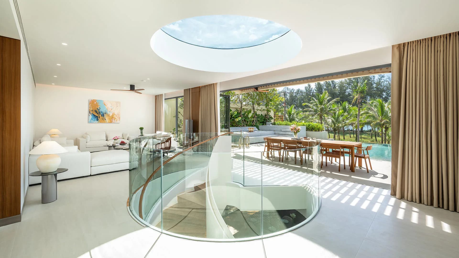 Open-plan villa living room with oval skylight, curved glass stair balustrade, terrace dining table and private pool