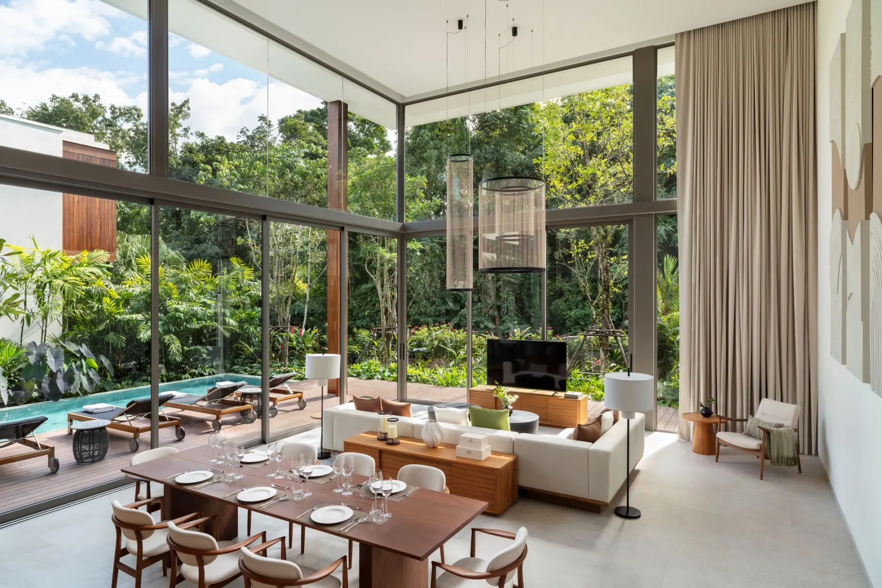 Living and dining room of a four-bedroom villa, glass on two sides, open to the pool terrace and the forest