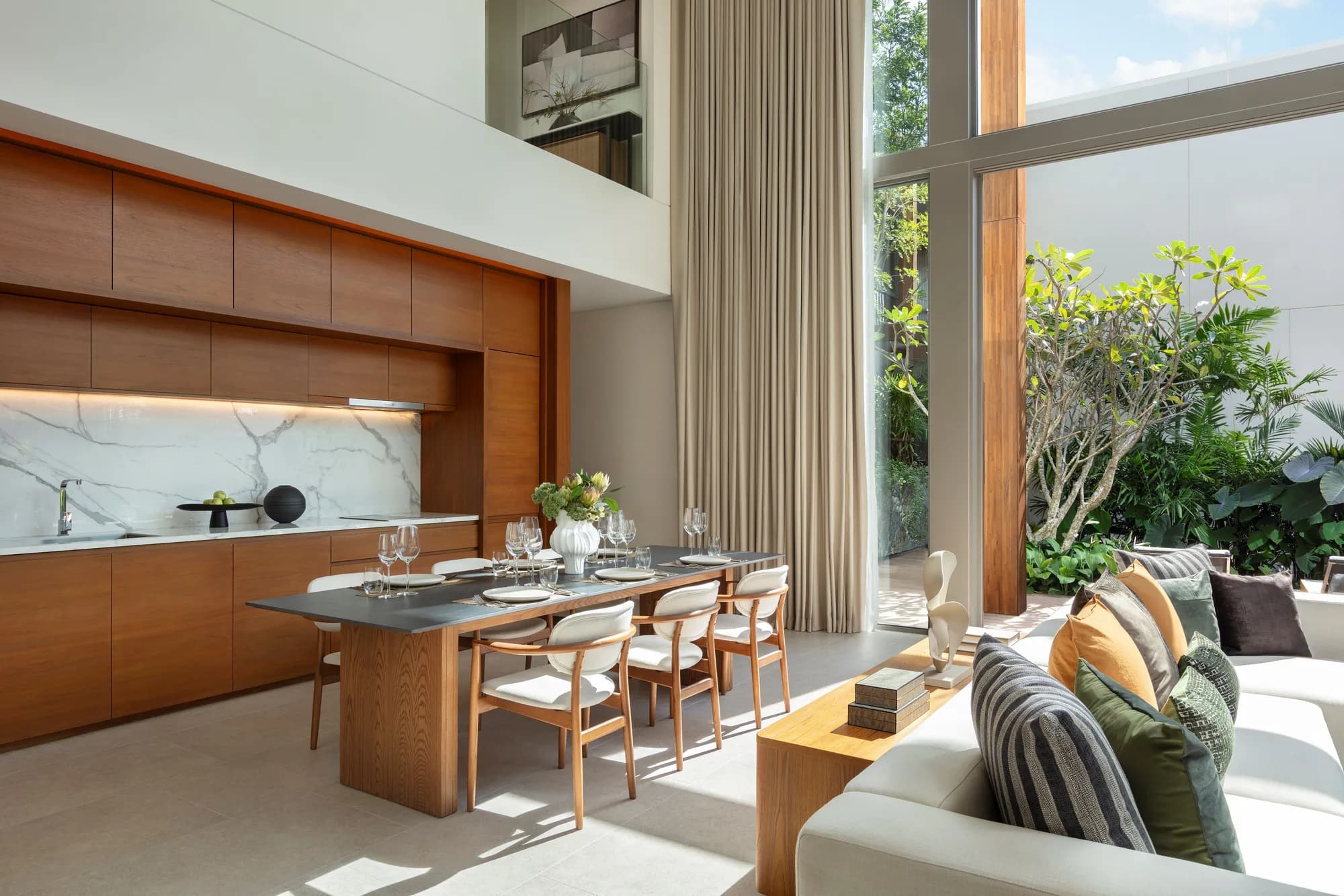 Dining table beside a timber kitchen wall with a marble splashback, a tall window onto the garden