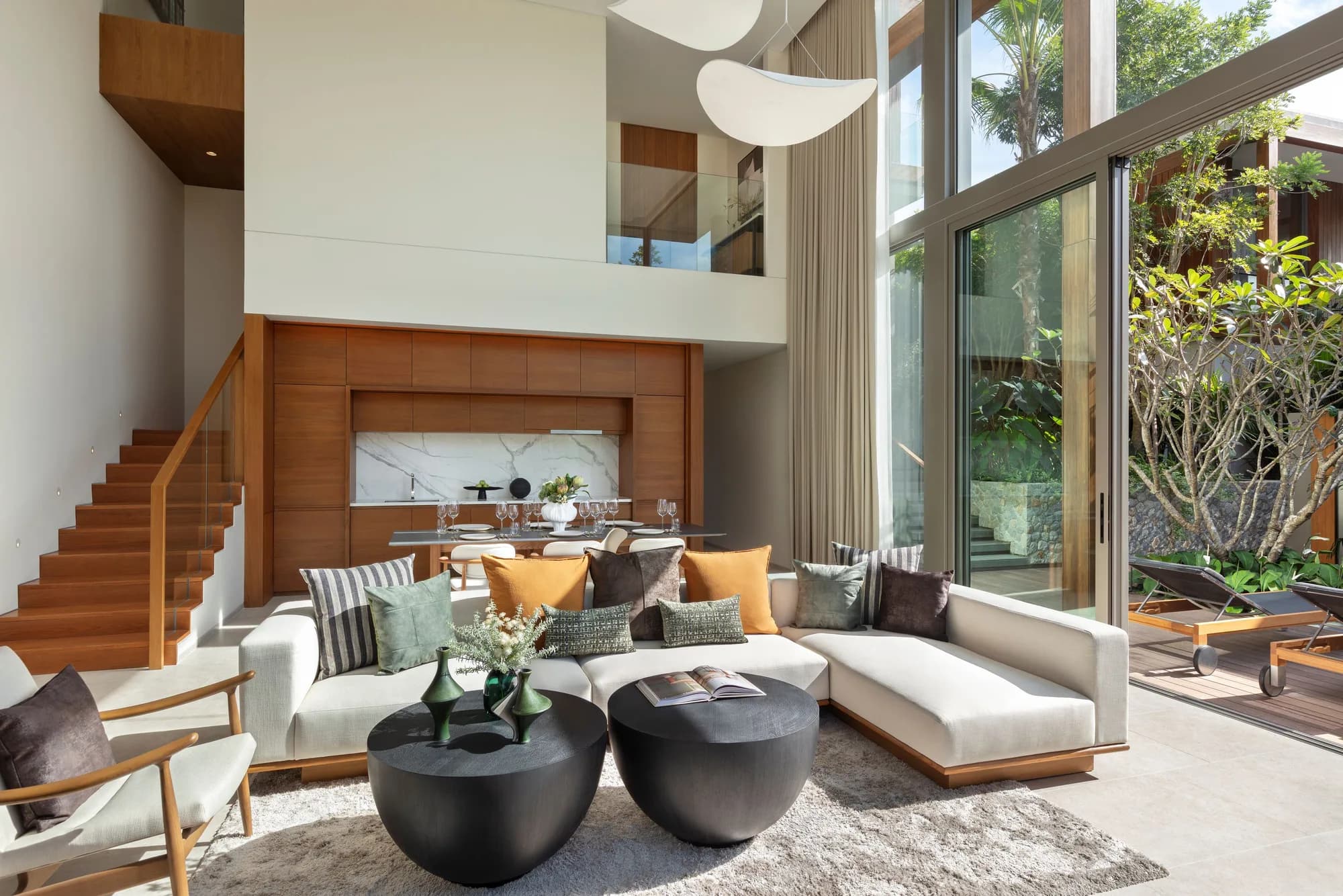 Double-height living room with a white sofa, a timber staircase and full-height glass onto the garden
