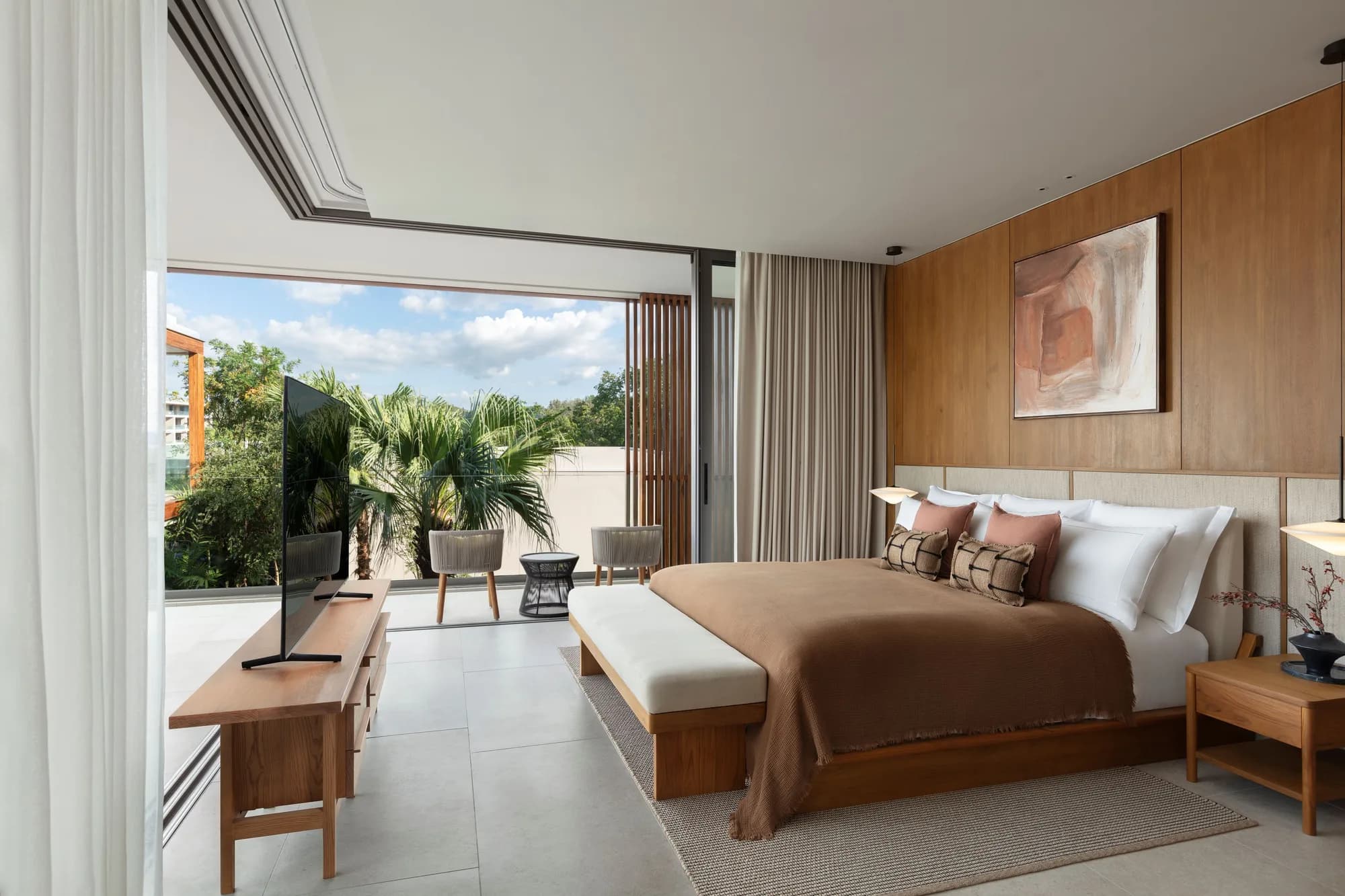 Principal bedroom with a timber headboard wall, glass sliders open onto a terrace with palms