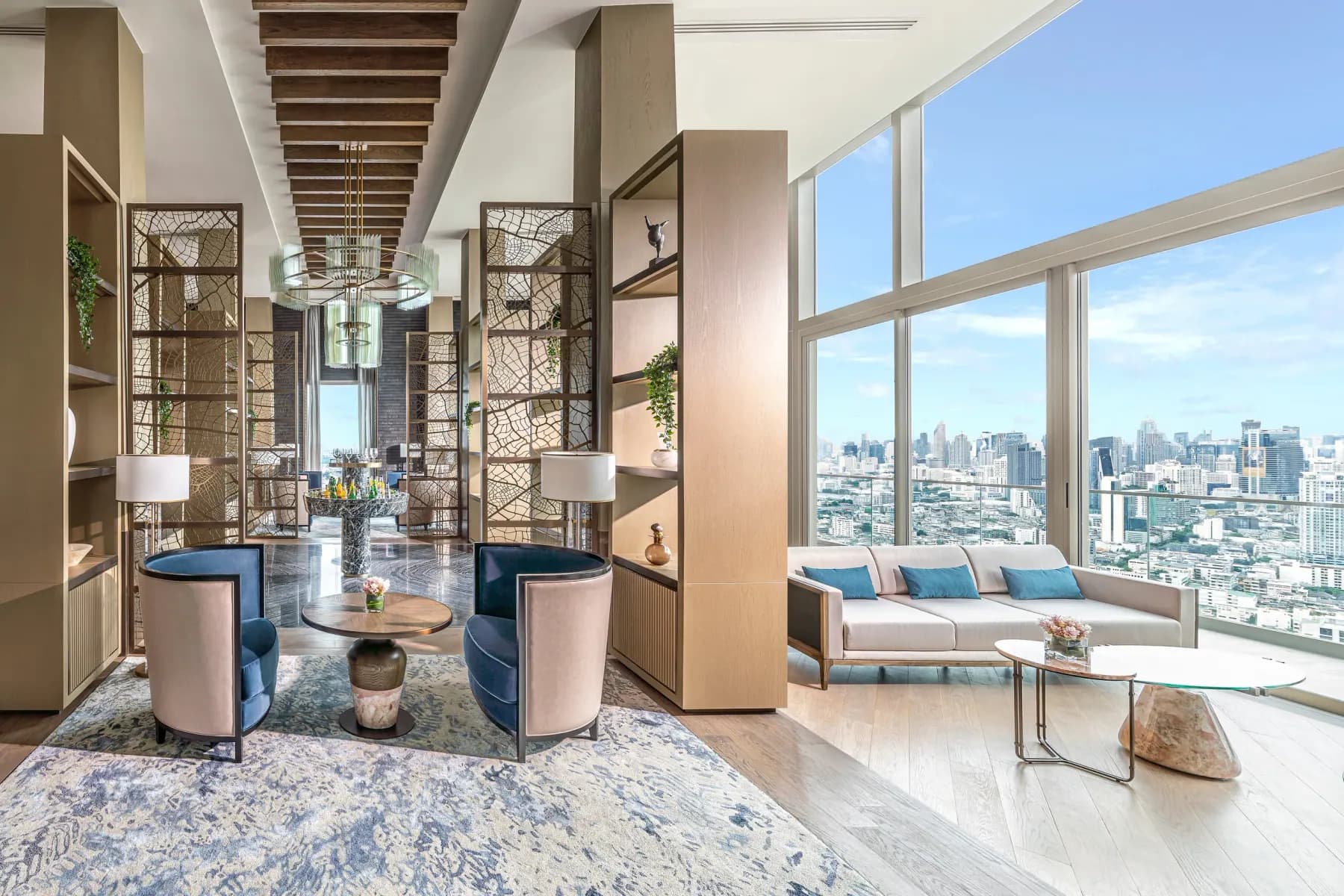 Residents' lounge with tub chairs, sofa and floor-to-ceiling glass overlooking the Bangkok skyline