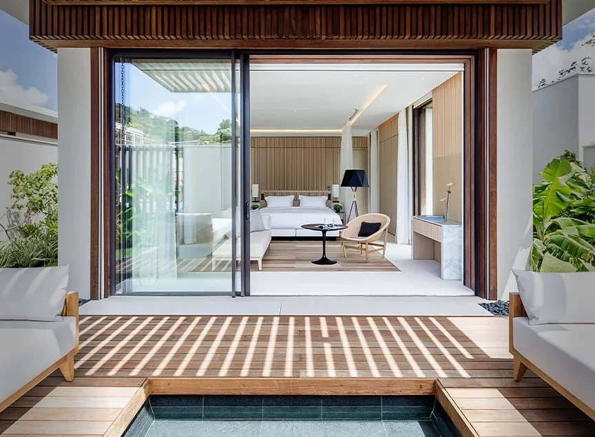 A bedroom pavilion in a four-bedroom beachfront villa at Silversands, its glass wall slid open onto a private deck and a planted courtyard.
