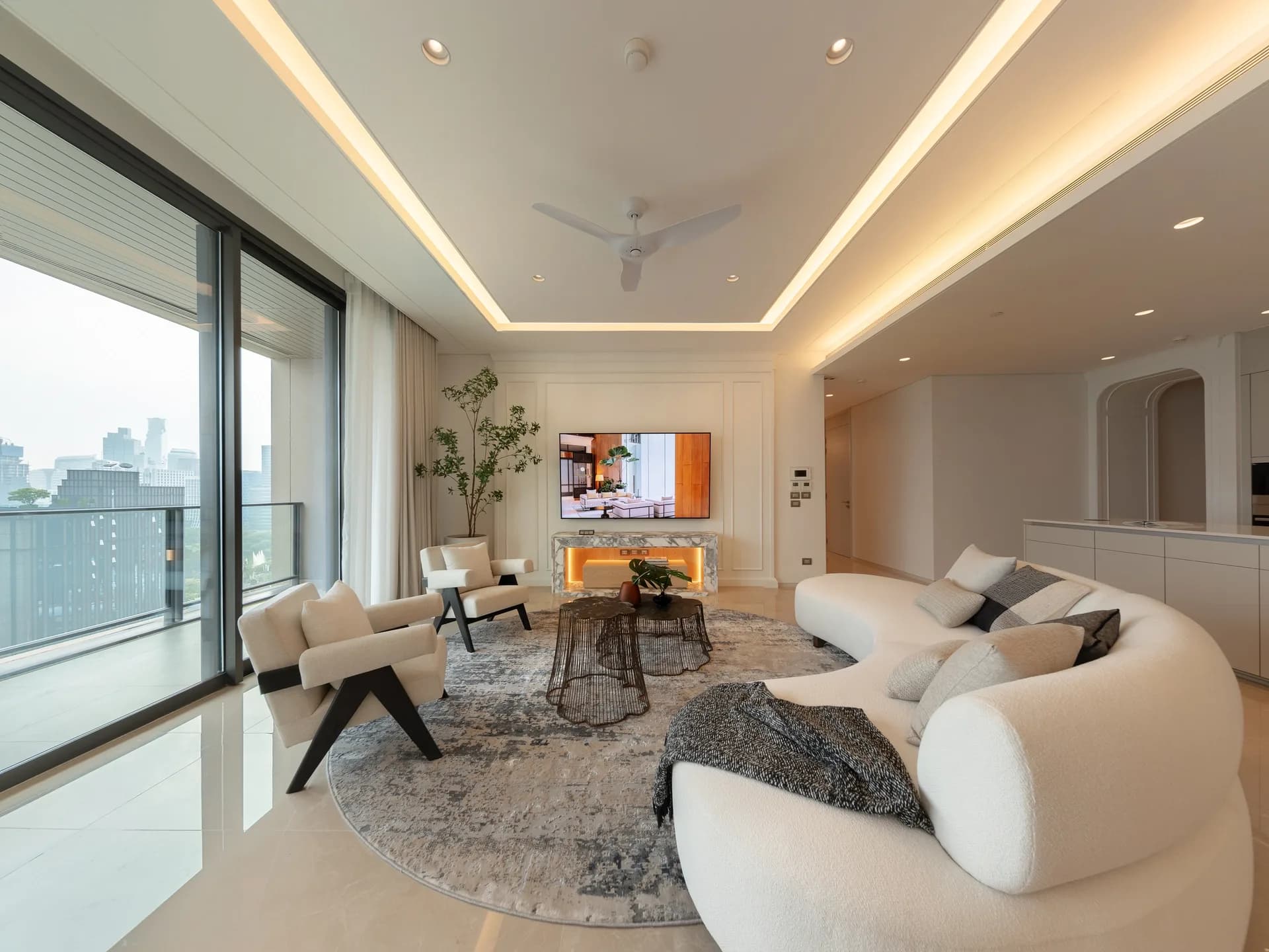 Living room of a residence with curved cream sofa, balcony glass and Bangkok skyline beyond.
