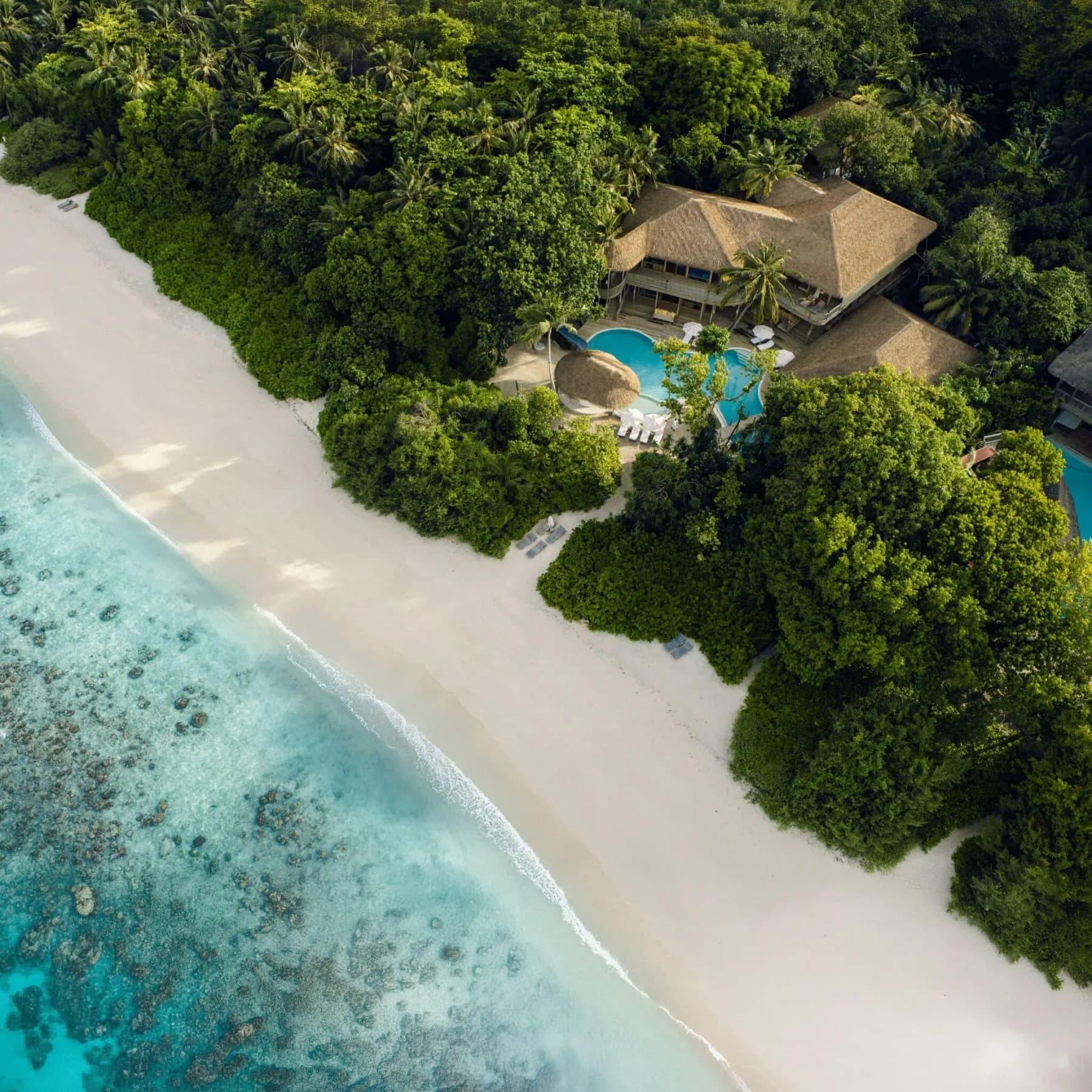 A Soneva Fushi private residence from above, its pool and thatched roofs set back from the beach in Baa Atoll.