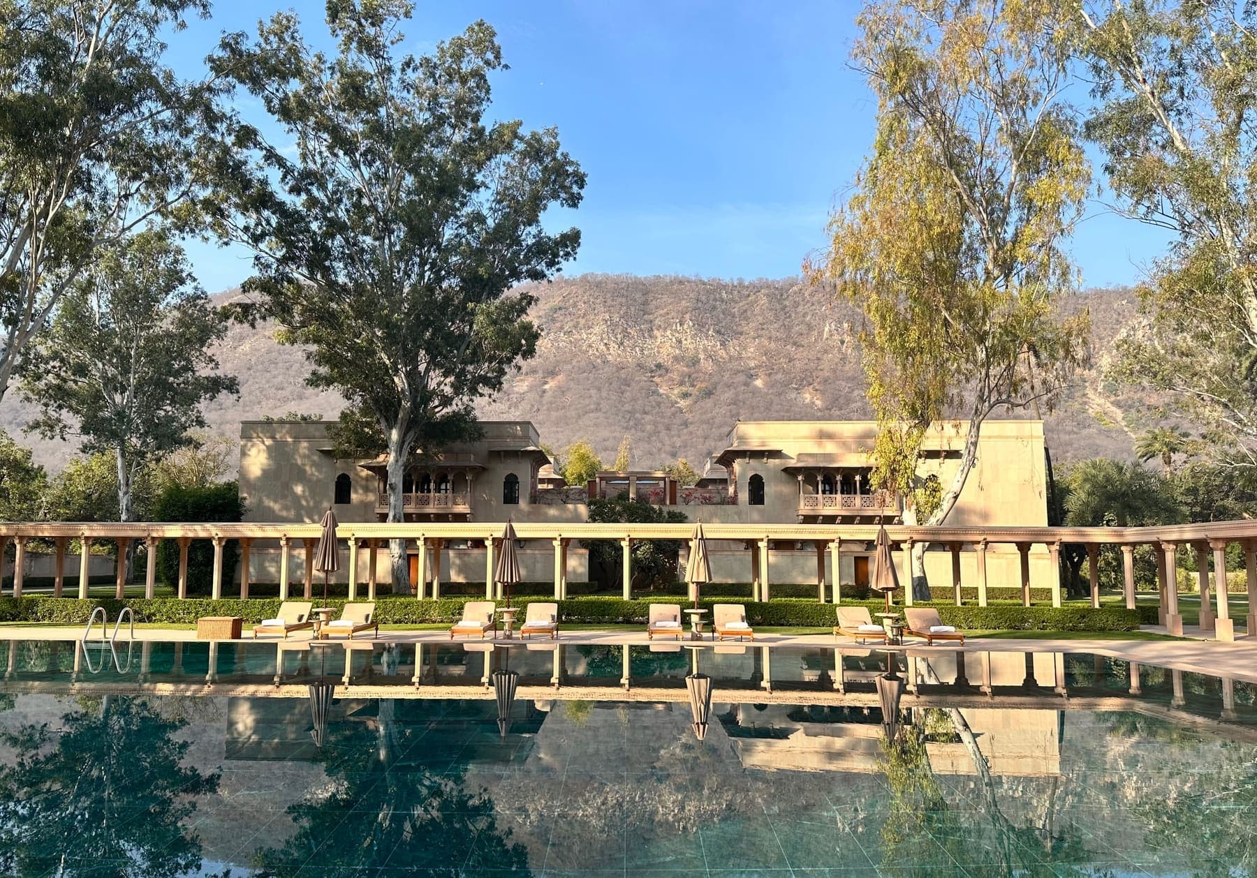 Длинный бассейн и колоннада Amanbagh в Раджастхане на фоне холмов Аравалли