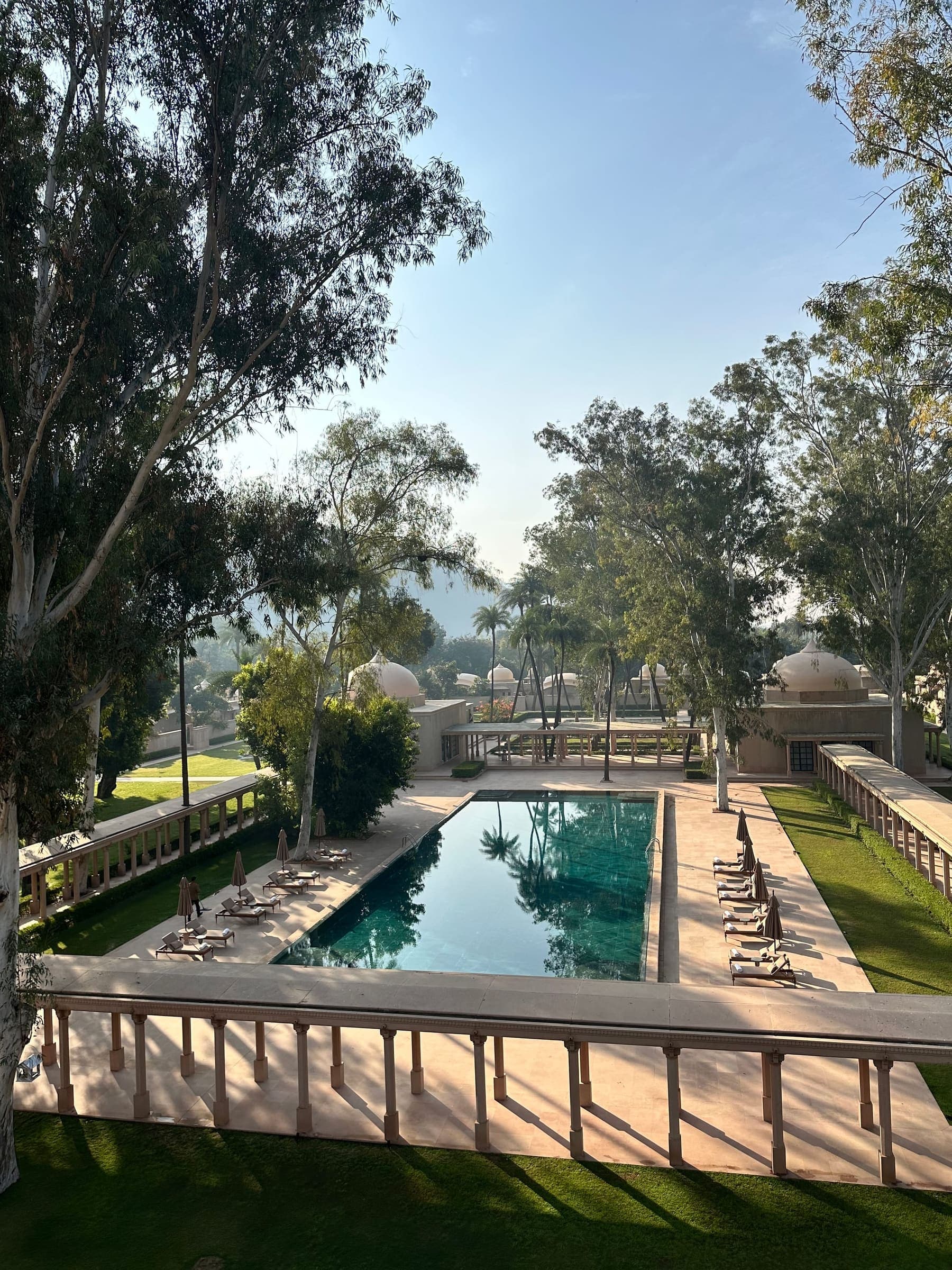 La larga piscina de Amanbagh vista desde una terraza alta, con tumbonas a ambos lados y pabellones con cúpula al fondo