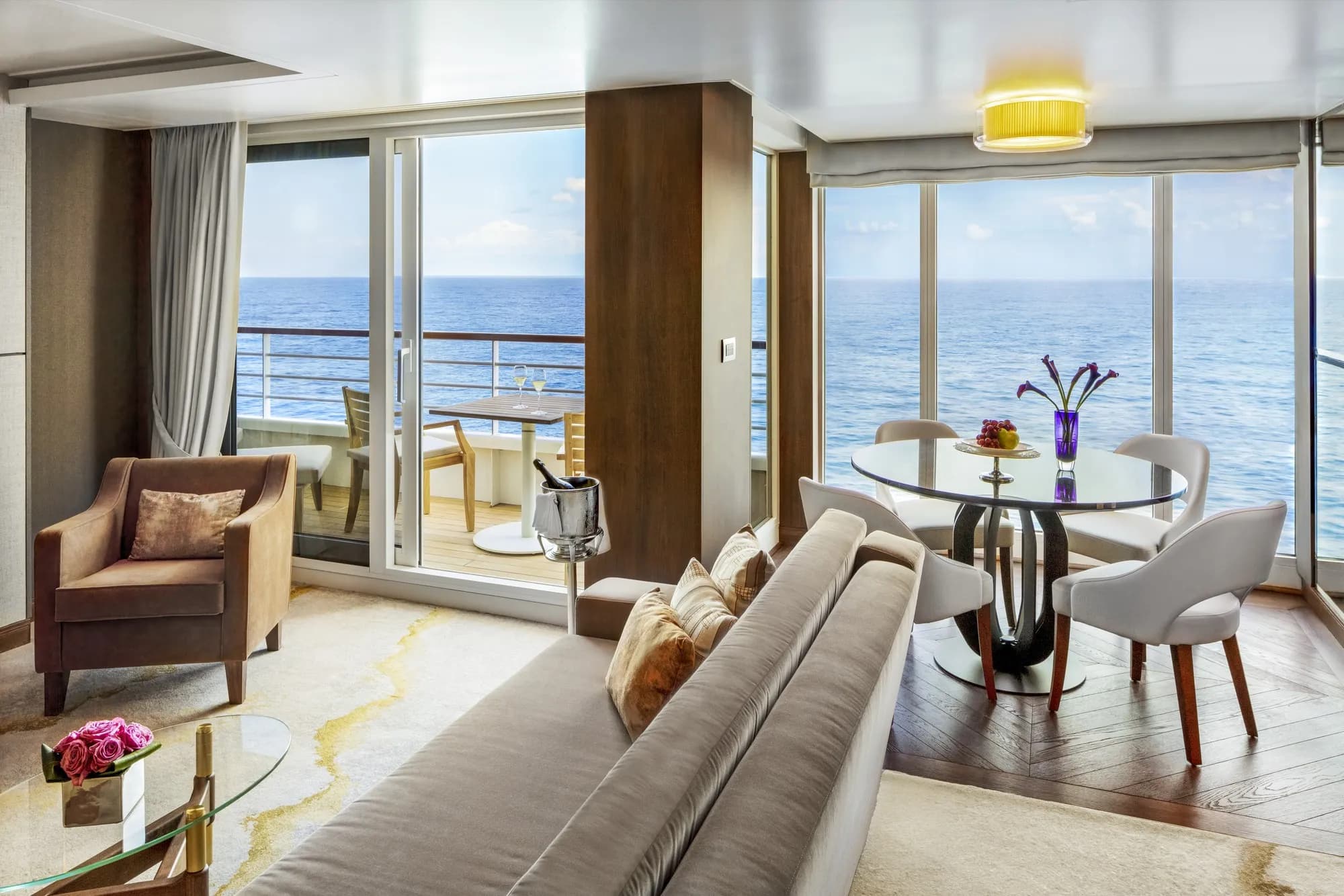 The living area of a Crystal Penthouse Suite, sofa and dining table by floor-to-ceiling windows, the veranda and open sea beyond