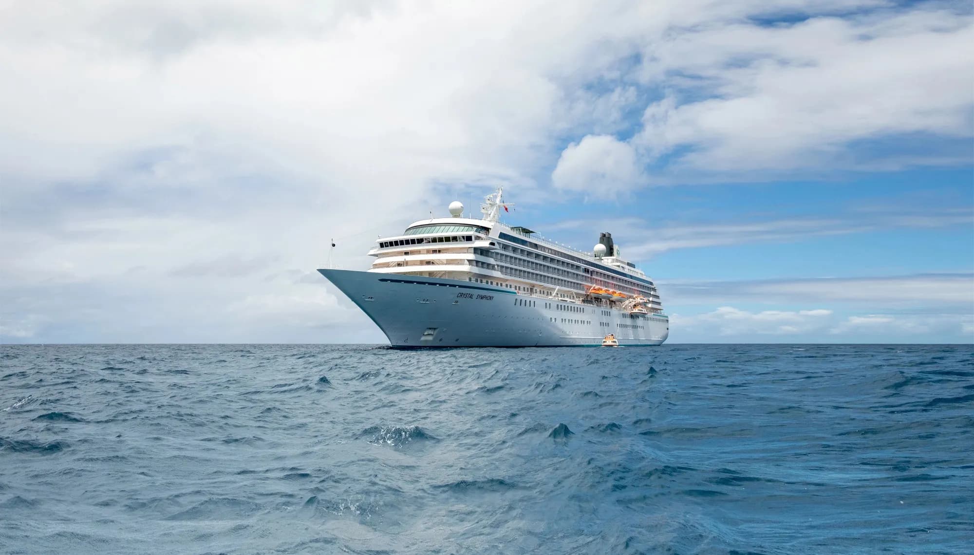 Crystal Symphony at sea under a broken sky, a tender alongside