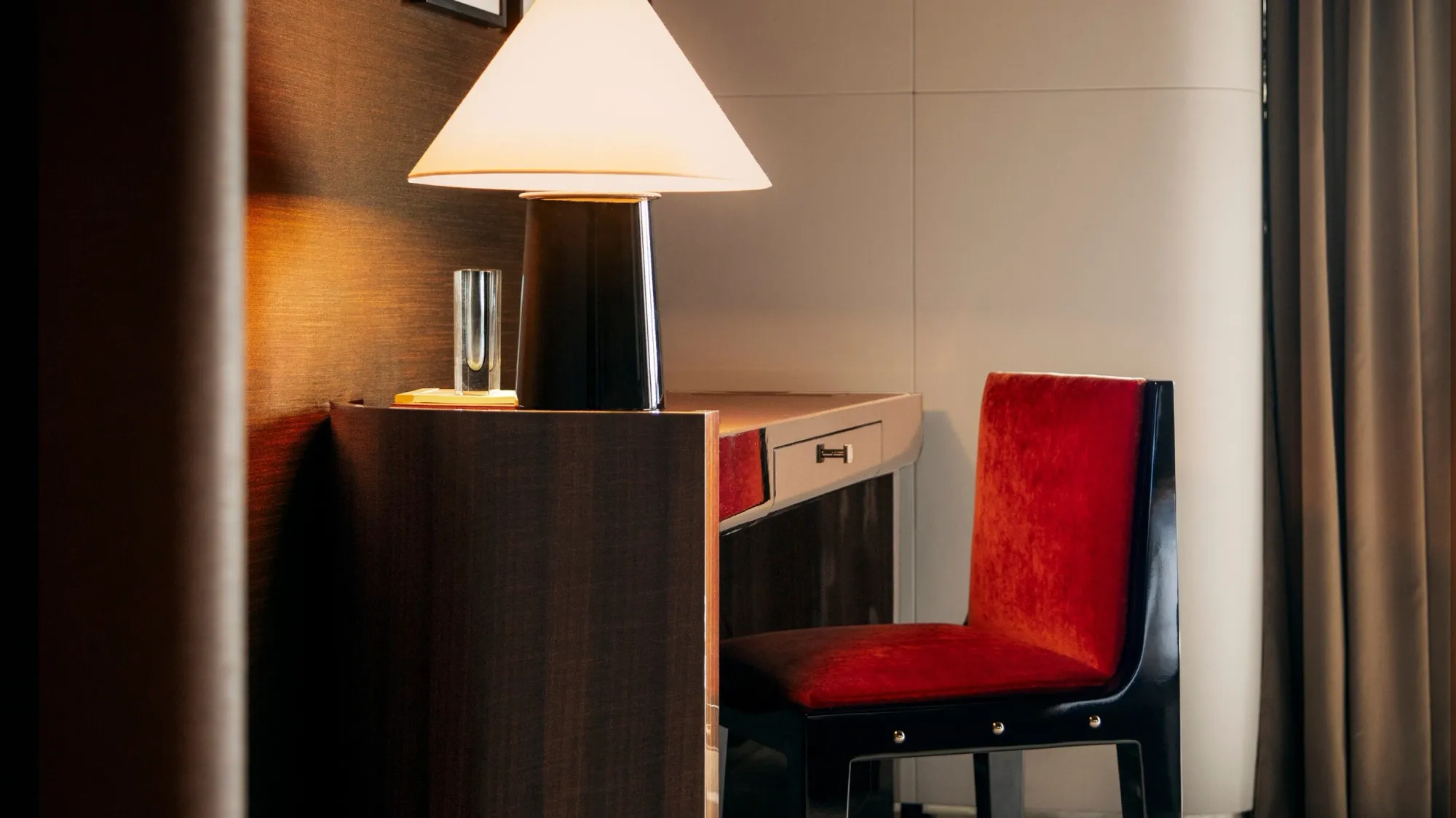 A writing desk in the Zephyr suite on Orient Express Corinthian: a cone-shaded lamp on the dark wood desk, a glass vase and a red velvet chair
