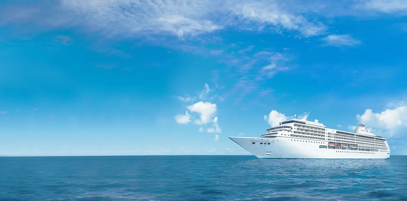 Seven Seas Mariner at sea under a blue sky with scattered clouds, her name on the bow