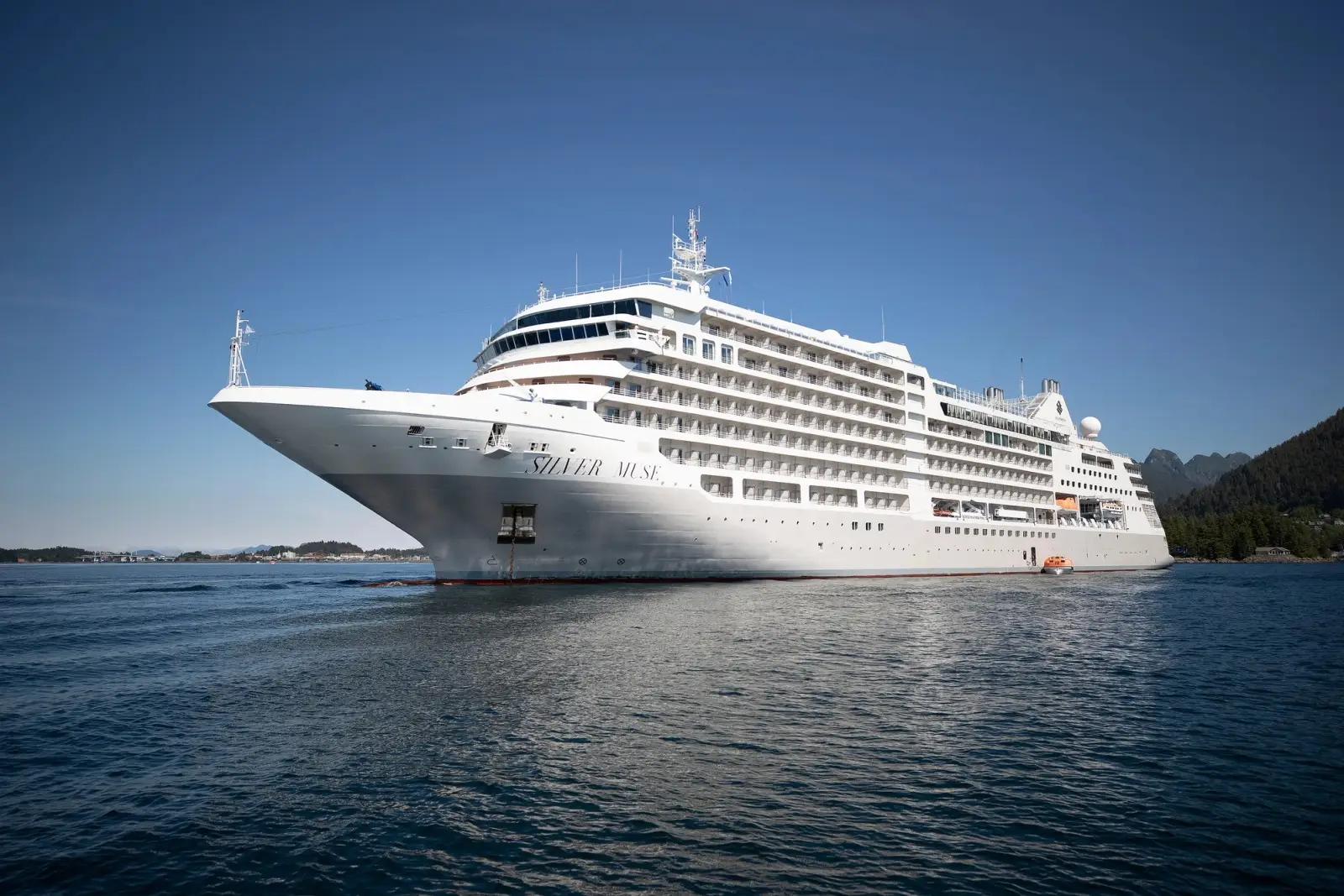 Silver Muse at sea, seen from off her bow, a wooded shore behind