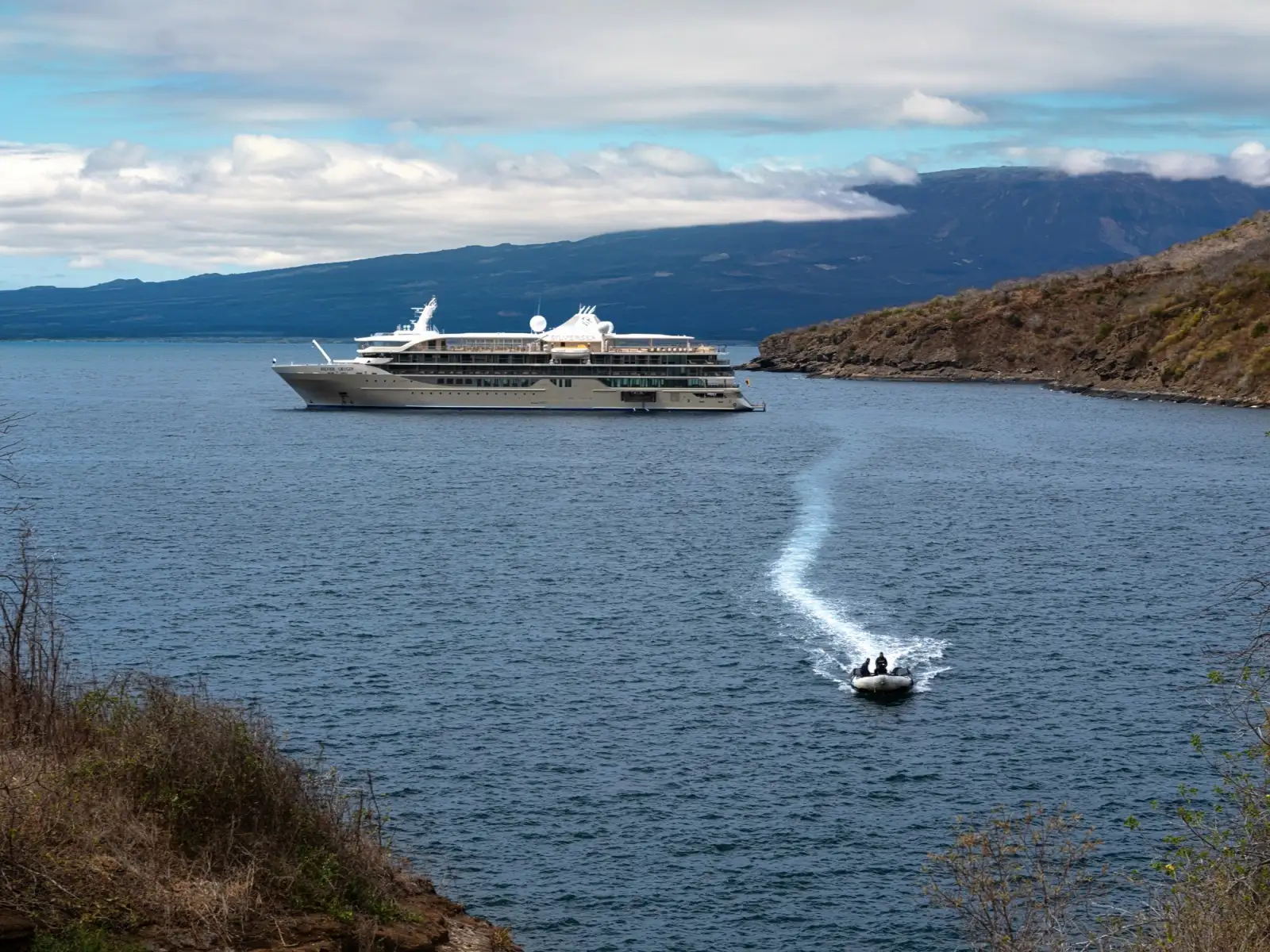 Silver Origin at anchor off a Galápagos island, a Zodiac crossing the bay in front of her