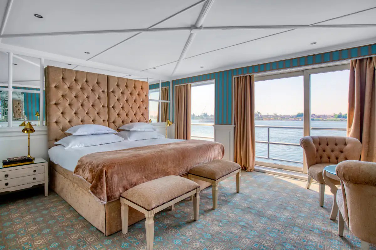 A Grand Suite on River Tosca, a tufted headboard and armchairs facing sliding doors onto the Nile