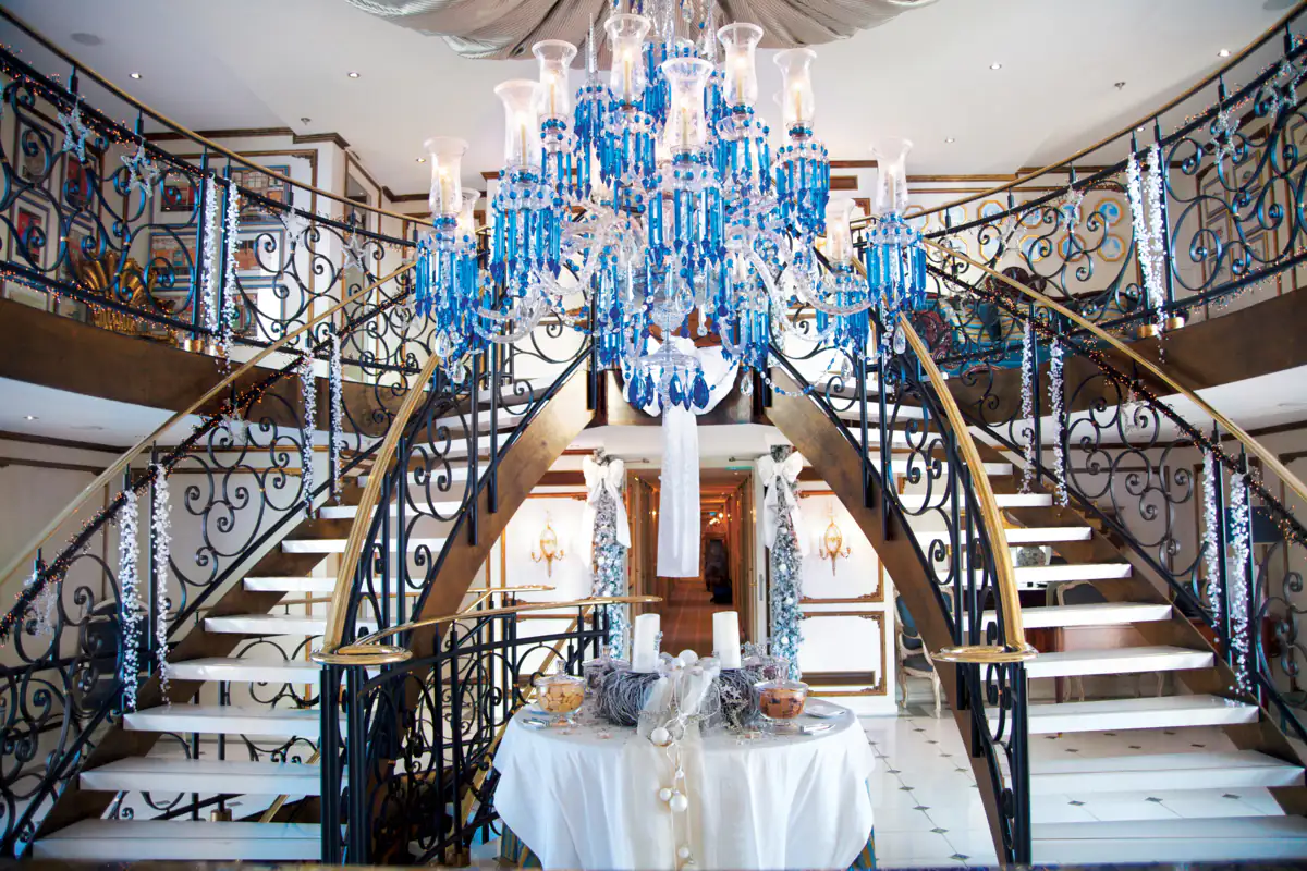 The two-storey foyer of S.S. Antoinette, twin curved staircases under a blue Baccarat chandelier, dressed for the holidays