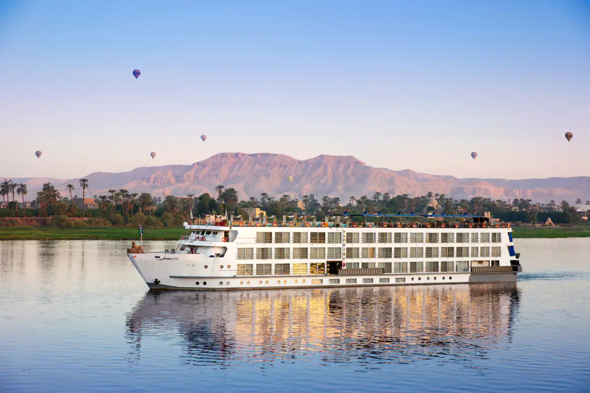 S.S. Sphinx on the Nile, hot-air balloons over the hills behind the palms