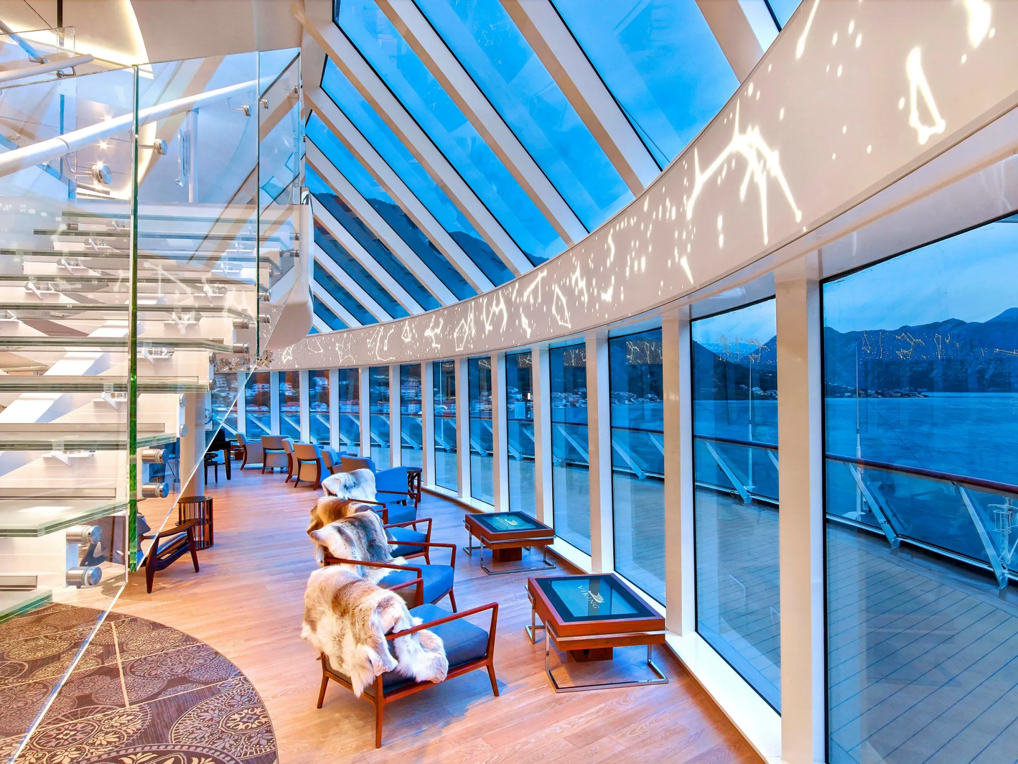 The Explorers' Lounge at dusk, armchairs with sheepskin throws along curved floor-to-ceiling windows
