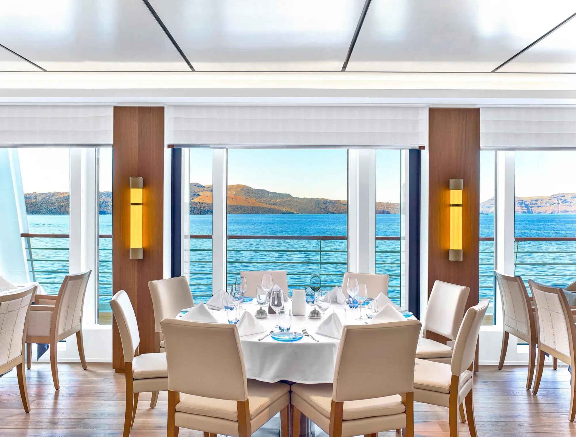 A table in The Restaurant on a Viking ocean ship, set in front of tall windows over the sea and a volcanic coast
