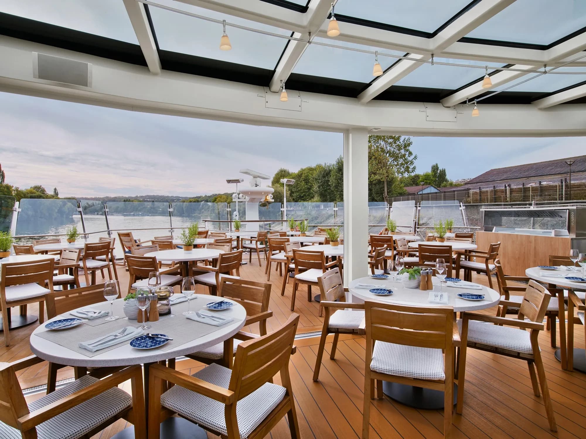 The covered Aquavit Terrace at the bow of a Viking Longship, tables set for a meal beside the river