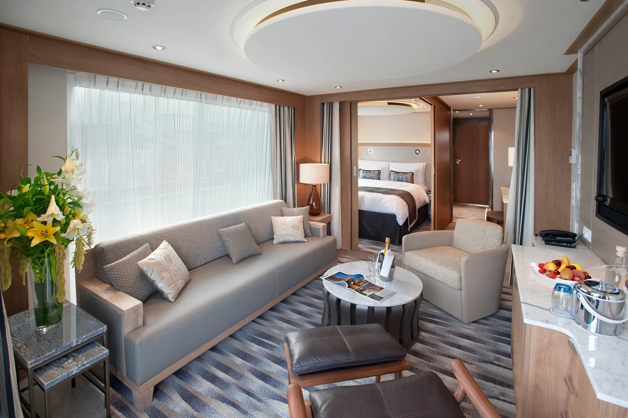 The sitting room of an Explorer Suite on a Viking Longship, a grey sofa and armchair, the bedroom through an open door