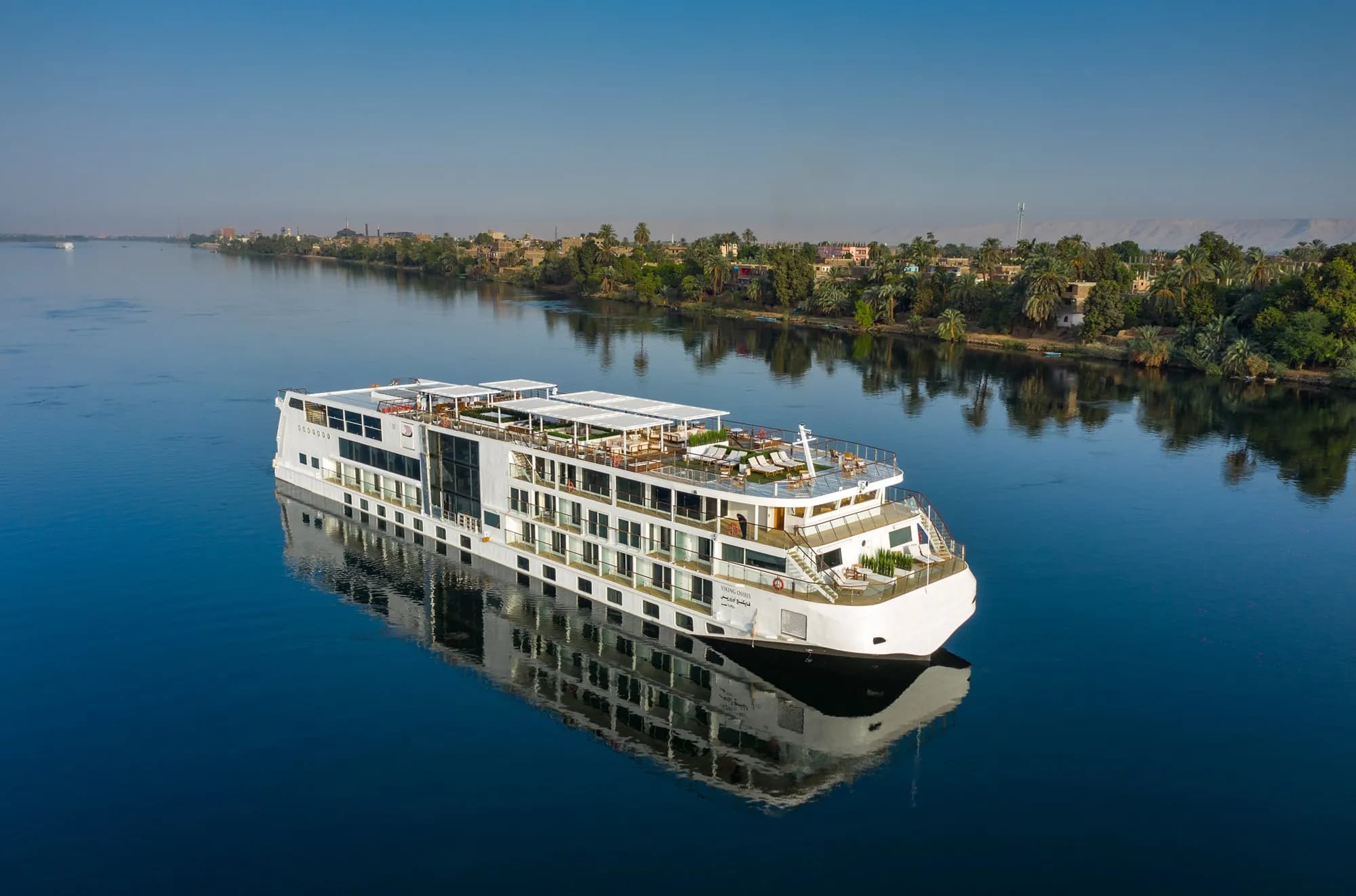 Viking Osiris on the Nile, seen from above, reflected in still water beside a palm-lined bank