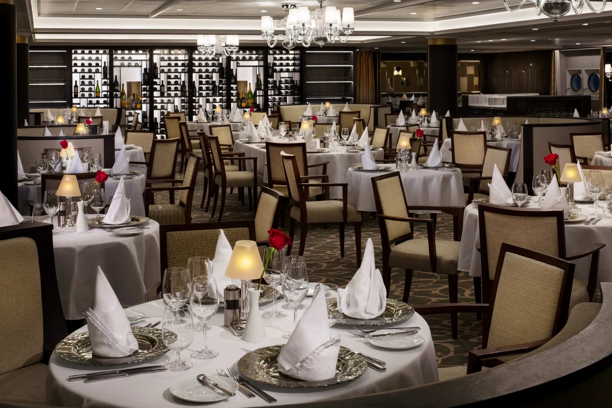 Amphora, the Windstar main dining room, round tables set for dinner in front of a backlit wine wall