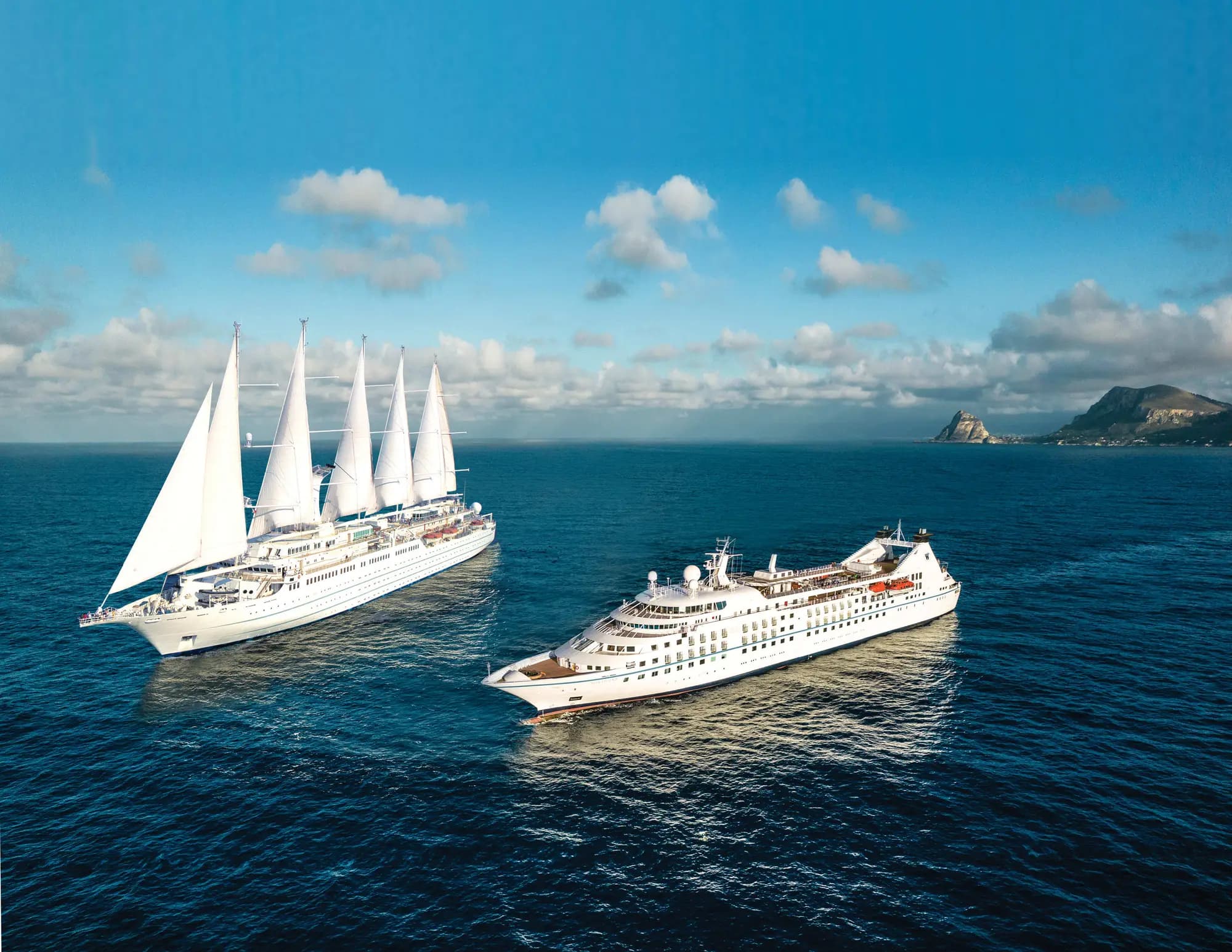 A five-masted Windstar sailing ship under sail beside an all-suite Windstar motor yacht on open sea