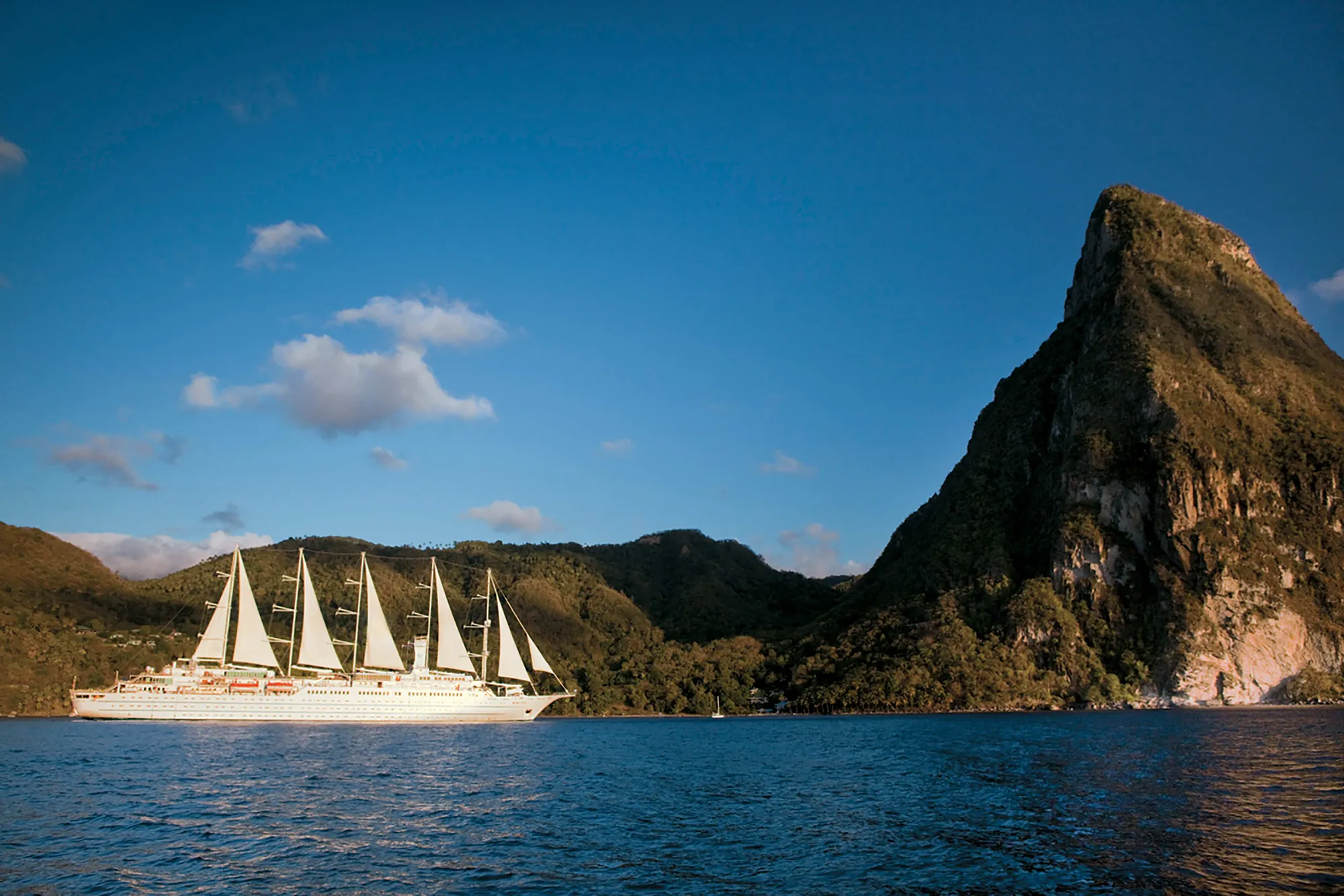 A five-masted Windstar sailing ship under full sail below one of St Lucia's Pitons in evening light