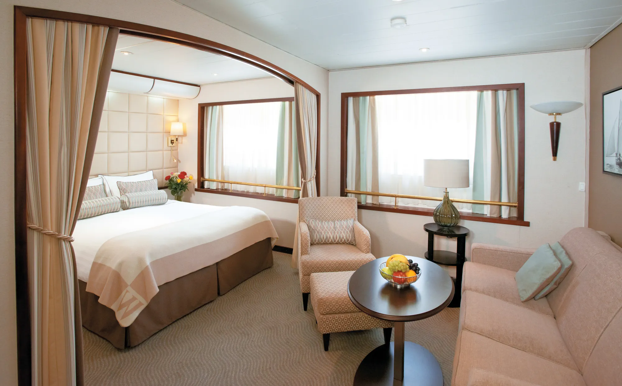A suite on Wind Surf, the bed in a curtained alcove, two picture windows with brass rails and a sitting area