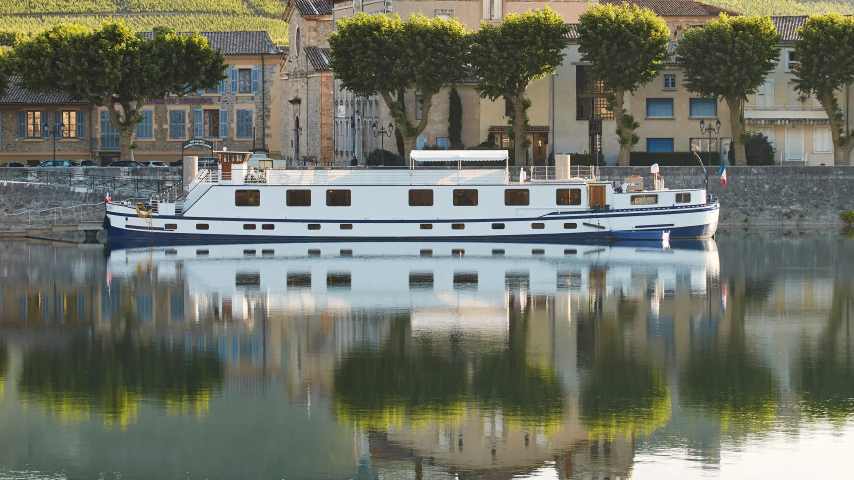 A Belmond hotel barge moored below a French village on the Rhône