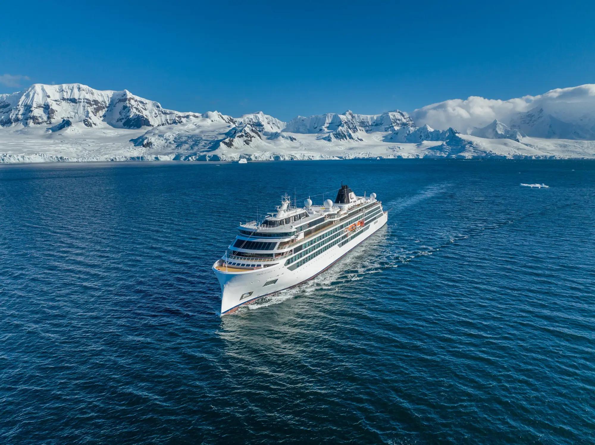 Viking Octantis under way in dark blue water below the snow-covered mountains of the Antarctic coast